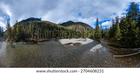 Crystal river winds through a pine forest with mountain peaks in BC, Canada.