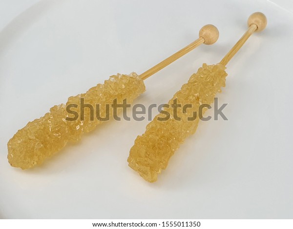 a\
Crystalline rock candy in wood swizzle sticks make for coffee or\
tea display on white plate in white\
background