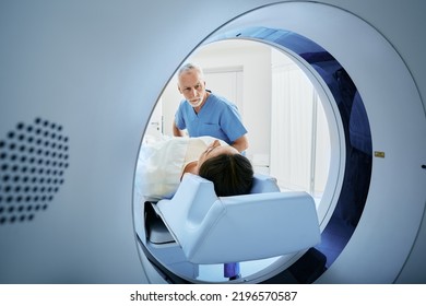 CT scan technologist overlooking patient in Computed Tomography scanner during preparation for procedure. Woman patient going into CT scanner