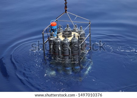 CTD rosette sampler with bathometers and other science equipment for measurement of underwater environment parameters like temperature, salinity and others. Sampler is half submerged in water.