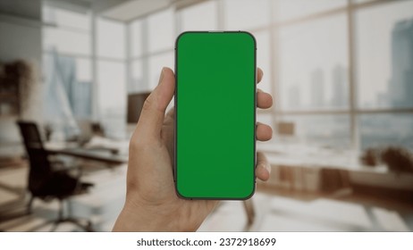 CU 30s Caucasian male holding a generic smart phone in vertical orientation, bright open space office in background, green screen chroma key - Powered by Shutterstock