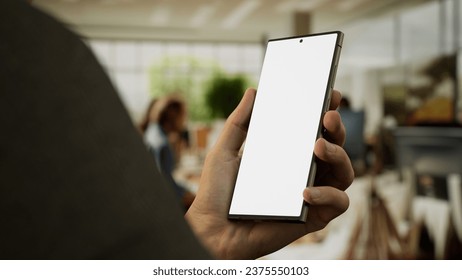 CU 30s Caucasian male holding a generic smart phone in vertical orientation, bright open space office in background, green screen chroma key