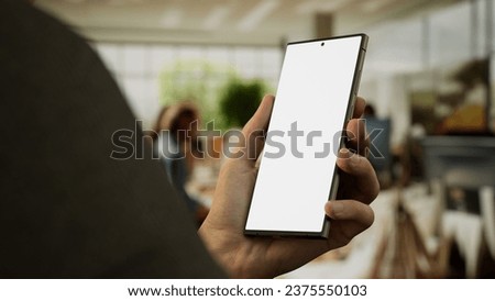 CU 30s Caucasian male holding a generic smart phone in vertical orientation, bright open space office in background, green screen chroma key