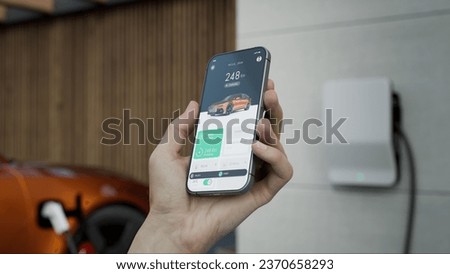 CU Caucasian man using EV application on his phone to check charging status. Private house in the background. Fictional application 