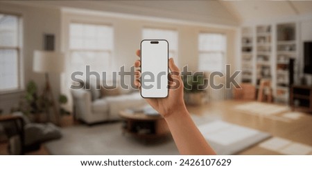 CU Caucasian man using his phone at home. Daytime shot, furnished house interior in the background. Blank screen, smartphone mockup