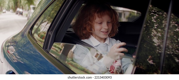 CU Portrait Of Little Kid Boy Using His Phone On The Back Seat While Taking A Ride To School. Shot With 2x Anamorphic Lens