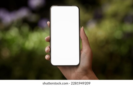 CU Silhouette of Caucasian female holding a generic smart phone in a right hand in vertical orientation, screen facing camera. Garden with green plants in the background - Powered by Shutterstock