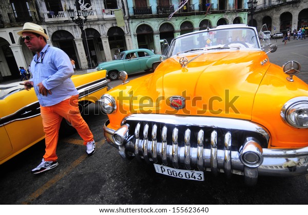CUBA, HAVANA - JUNE 27, 2013: Luxury renovated\
old American car in front of the hotel. Classic cars are still in\
use in Cuba and old timers have become an iconic view and a\
worldwide known\
attraction