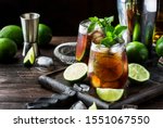 Cuba libre alcohol cocktail with golden rum, lemon juice, cola, lime and ice, dark bar counter background, bar tools, place for text