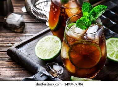 Cuba libre alcohol cocktail with golden rum, lemon juice, cola, lime and ice, dark bar counter background, bar tools, place for text - Shutterstock ID 1498489784
