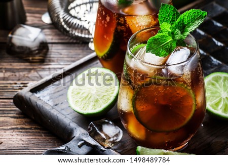 Cuba libre alcohol cocktail with golden rum, lemon juice, cola, lime and ice, dark bar counter background, bar tools, place for text