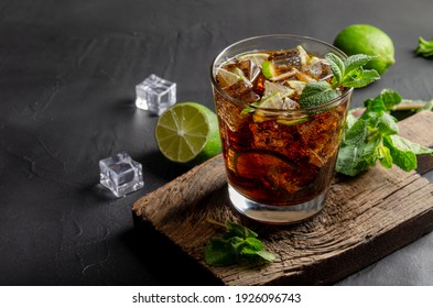 cuba libre, rum and cola cocktail in glass with a lime and mint on black background