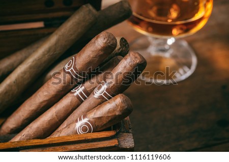 Cuban cigars in a wooden box, blur glass of cognac brandy, closeup view with details, copy space