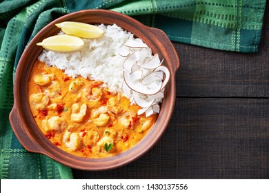 Cuban Dish Baracoa: Large Shrimps In Unsweetened Coconut Milk Sauce With Coconut Chips On Top, Served With White Rice, In A Rustic Clay Pot On A Wooden Table, Close-up, Copy Space, Horizontal View