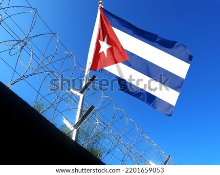 The Cuban flag hangs in the cloudy sky outside the prison's barbed wire. waving in the sky