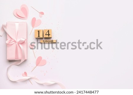 Cube calendar with date 14 FEBRUARY, gift box and paper hearts for Valentine's Day celebration on white background