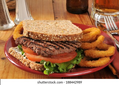 A Cube Steak Sandwich With Onion Rings On Sprouted Nut And Seed Bread