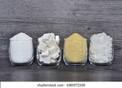 Cube sugar, raw sugar , crystalline sugar and granulation sugar in clear glasses with grey wooden background