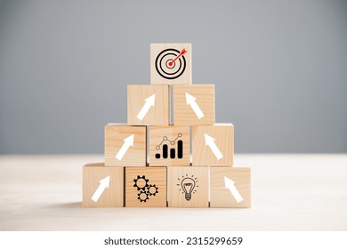 Cube wood blocks arranged with Target icon on top rise up arrows, representing growth. Bar graph chart steps on vertical symbolize a business growth process, signifying profit, investment, economic - Shutterstock ID 2315299659