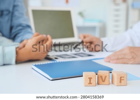 Cubes with abbreviation IVF on table against couple visiting fertility doctor in clinic, closeup