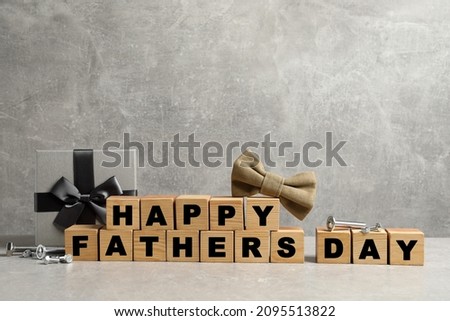 Cubes with phrase Happy Father's Day, bow tie and gift box on grey background. Space for text