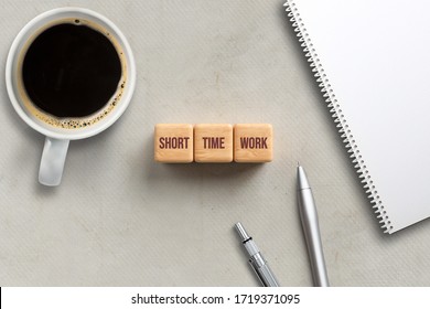 Cubes Showing Message SHORT TIME WORK With Coffee, Pens, And Notepad On Paper Background