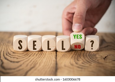 cubes with the word "SELL" and hand turning a cube with answer "yes" and "no" on wooden background