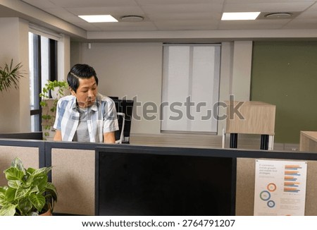Cubicle worker glancing at pinned chart and activating animated rings on monitors, showing data. Workstation, screens, openplan, plants, greenery, office, minimalist