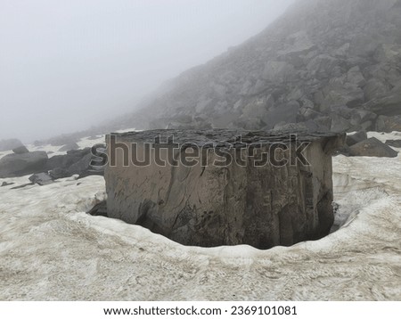A cuboidal or cylindrical rock structure surrounded by hard snow on high altitudes of Himalayas. The photo was captured during trek to Kalihani Pass near Manali in Himachal Pradesh, India.