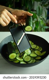 Cucumber sliced with a mandolene. Thinly sliced cucumbers with male hand in the kitchen.