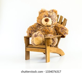 Cuddly Stuffed Brown Bear Sitting In A Rustic Wooden Adirondack Chair Isolated On White