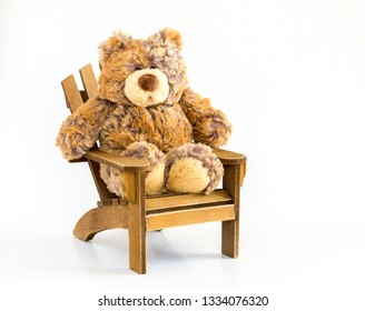 Cuddly Stuffed Brown Bear Sitting In A Rustic Wooden Adirondack Chair Isolated On White