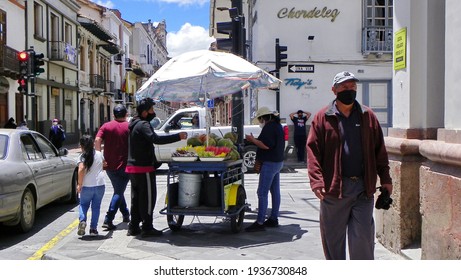 Cuenca, Ecuador - February 7, 2021: Street vender with moving cart  offers fruit, watermelons and coco nuts at historical part of city Cuenca. People in protective masks during pandemic