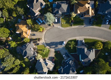 A Culdesac In A Residential Neighborhood With Houses, Parked Cars, Trees, And Grass Lawns.