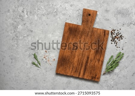 A culinary backdrop with an empty cutting board, rosemary, salt, and peppercorns. Top view, flat lay, copy space. Rustic gray background with cooking ingredients.