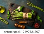 Culinary background of asparagus preparation. Bunches of asparagus on a wooden board. On a dark stone background. Top view.