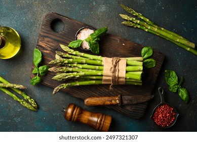 Culinary background of asparagus preparation. Bunches of asparagus on a wooden board. On a dark stone background. Top view.