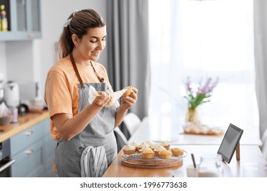 culinary, bake and cooking food concept - happy smiling young woman with baking bag making cupcake topping on kitchen at home