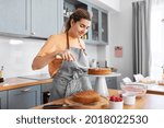 culinary, baking and cooking food concept - happy smiling young woman making layer cake on kitchen at home