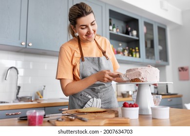 culinary, baking and cooking food concept - happy smiling young woman making layer cake and spreading topping cream on kitchen at home