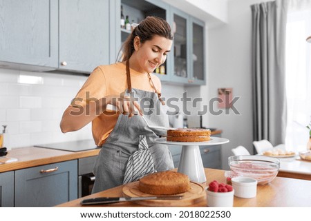 culinary, baking and cooking food concept - happy smiling young woman making layer cake on kitchen at home