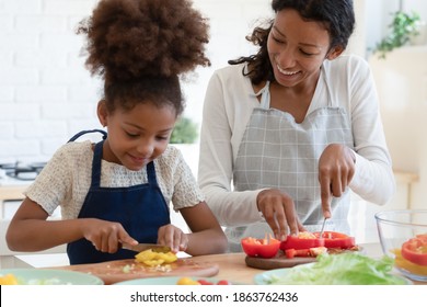 Culinary is easy. Inspired happy african american mother and tween daughter prepare vegan food, grown elder and small younger sisters trying new cooking recipe, cutting vegetables talking at kitchen - Powered by Shutterstock