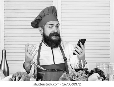 Culinary Education Online. Elearning Concept. Man Chef Searching Internet Recipe Cooking Food. Chef Smartphone Watch Culinary Show. Culinary School. Hipster In Hat And Apron Learning How Cook Online.