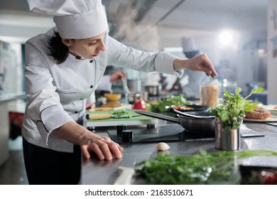 Culinary expert putting fresh chopped herbs in pan while cooking gourmet dish for dinner service at fine dining restaurant. Head chef preparing organic meal in professional kitchen. - Shutterstock ID 2163510671