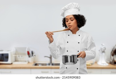 culinary and people concept - female chef in toque with saucepan and spoon cooking and tasting food over kitchen background - Powered by Shutterstock