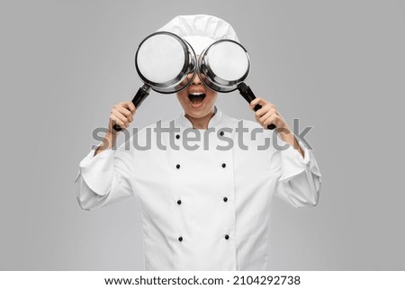 culinary and people concept - female chef in toque and jacket with saucepans having fun over grey background
