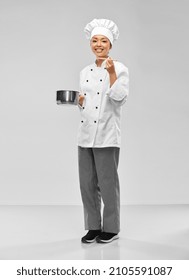 culinary and people concept - happy smiling female chef in toque and jacket with saucepan cooking food over grey background