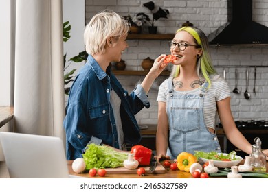 Culinary tutorial on laptop.Happy passionate lovable lgbtq female couple lesbians preparing food cooking dinner romantic lunch salad at home kitchen, trying vegetables and having fun. Love and passion - Powered by Shutterstock - Get 15% off with code: PIKWIZARD15