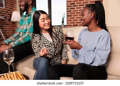 Cultural Diverse Nationalities, Ethnicities Women Couple Chatting, Talking, Discussing Happily During House Friends Gathering, Drinking Wine, Eating Bread Sticks, Cheese.