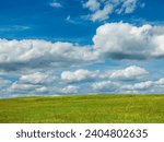 Cumulus clouds drifting across blue sky above a grassy hilltop field in a community park and conservation area on a summer afternoon